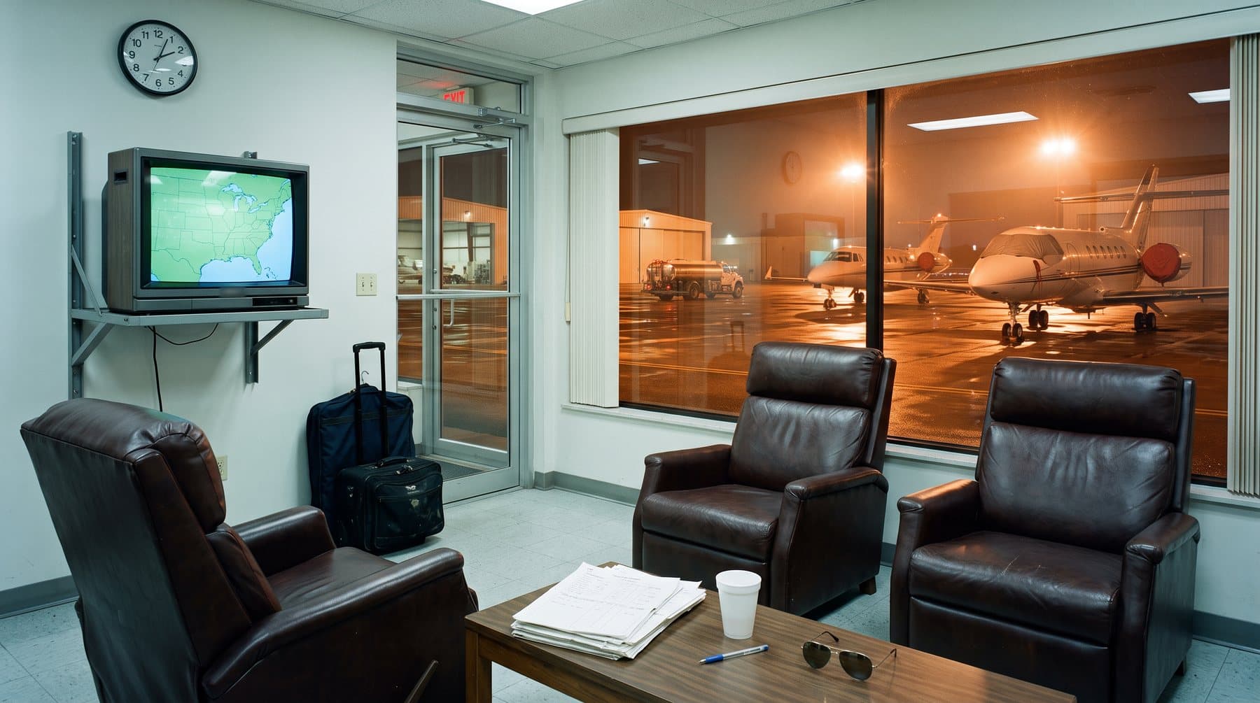 An empty airport crew lounge at night with vinyl chairs, a television and a window onto a floodlit ramp